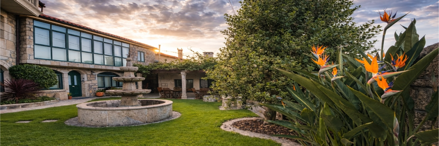 Vista general del jardín con fuente de piedra y mobiliario de exterior en Apartamentos Río Sil.